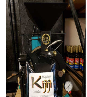 Bag of Kijiji Snicker Nut Coffee in front of a coffee roaster