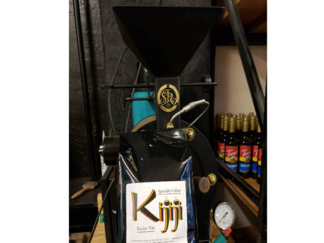 Bag of Kijiji Snicker Nut Coffee in front of a coffee roaster