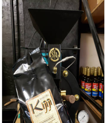 Bag of Kijiji Tanzania Blend Coffee in front of a coffee roaster