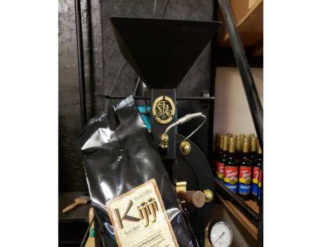Bag of Kijiji Tanzania Blend Coffee in front of a coffee roaster